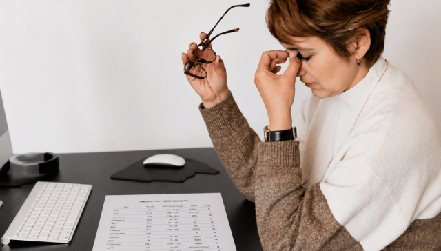Exhausted woman reviewing normal blood test results while sitting at her desk.