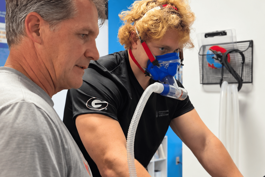 Client wearing an oxygen mask while riding a stationary bike during a monitored oxygen training session at O2 Performance and Recovery.